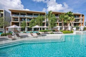 a swimming pool with chairs and umbrellas in front of a building at Wyndham Grand Nai Harn Beach Phuket in Nai Harn Beach