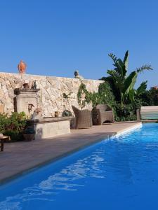 a swimming pool with wicker chairs next to a stone wall at LA MAISON DE JUSTINE in Grimaud