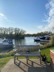 a wooden bench sitting next to a river with boats at The River Thames - Surrey Boat in Thorpe