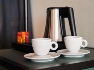 two white cups and saucers on a table with a coffee pot at Novotel Barcelona City in Barcelona