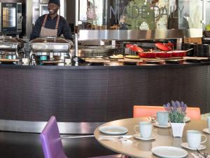 a man standing in a kitchen with tables in a restaurant at Novotel Barcelona City in Barcelona