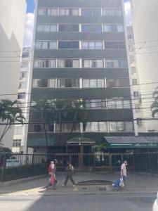 a group of people crossing a street in front of a tall building at Barra Apart in Salvador