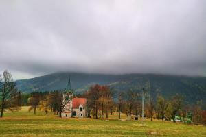 a church in a field with a mountain in the background at Malé Labe - ubytování v podkroví in Prosečné