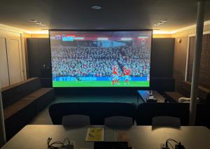 a room with a large screen with a soccer game at BIEI TERRACE 1st Floor - 1F専用独立玄関 - 1F占有78平米大型ワンルーム- ソファベッド7台, 170型米Valerion社製最新シアター動画視聴, 無料Wi-Fi, シャワー, ミニキッチン付き - 駅前通り沿い - in Biei +19 photos