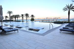 a swimming pool with lounge chairs and palm trees at Address Beach Resort Properties Bahrain in Manama