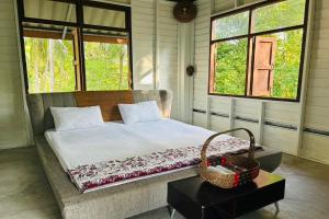 a bed in a room with two windows and a basket at Baan Nai Bang in Suratthani