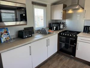 una cucina con armadi bianchi e un forno a piano cottura nero di Fantasy Island Holiday Park Eastgate - The Seasons with Hot Tub - Coastal Caravan Breaks a Ingoldmells Altre 12 foto
