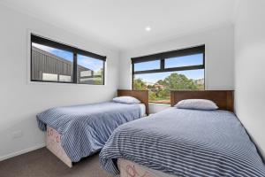 two beds in a room with two windows at Edinburgh Escape - Waihi Beach Holiday Home in Waihi Beach