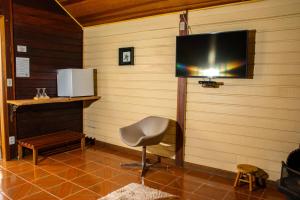 a room with a television on a wall with a chair at Pousada Olivier da Montanha in Santo Antônio do Pinhal