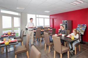 a man standing in a dining room with people sitting at tables at Appart'hôtel Odalys City - Orléans Centre in Orléans +56 photos