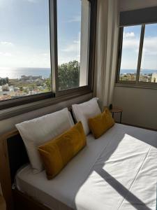 a bed with two pillows in a room with windows at Kissonerga Sea Breeze Apartments Panoramic Ocean View in Kissonerga