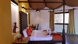 a bedroom with a canopy bed with white sheets and red pillows at Palash Kothi -Bandhavgarh in Tāla