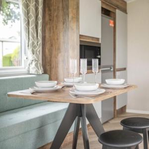 Una mesa de madera con platos y copas de vino encima. en Gimblet Rock Holiday Park, en Pwllheli