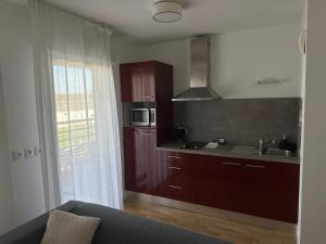 a kitchen with red cabinets and a sink and a couch at Domitys Le Chant des Lavandières in Vernouillet