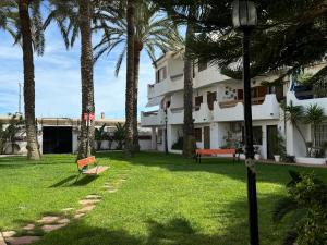 a building with palm trees and a bench in the grass at Puebla de Farnals playa- Oasis Apartments - Costa de Valencia Beachside Stay in Puebla de Farnals