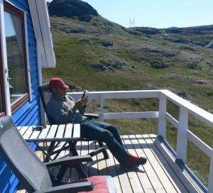 a man sitting on a deck reading a newspaper at Isikkivik Cottage in Narsaq