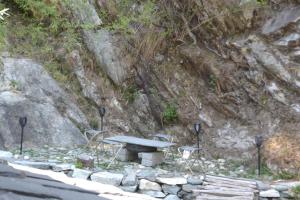 a picnic table and chairs in front of a rock wall at Moksha By The River,Jibhi in Jibhi