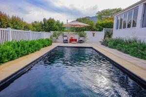 a swimming pool in a backyard with an umbrella at The Hedge Cottage in Riebeek-Kasteel