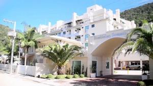 a large white building with palm trees in front of it at Apartamento 207 varias piscinas in Bombinhas