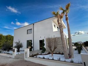 a white house with palm trees in front of it at Primosten Hills West - Branded Luxury Villa in Primošten