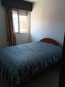 a bedroom with a bed with a blue comforter and a window at Apartamento en Paysandu in Paysandú