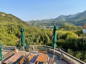 a wooden table with chairs and umbrellas on a balcony with mountains at Skadar Lake Family Resort in Rijeka Crnojevića