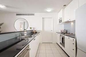 Una cocina blanca con fregadero y espejo. en Cozy 2BR Apartment Steps from Darling Harbour, en Sídney