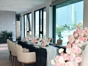 a long table with pink roses on it in a room with windows at Cicilia City Hotel Saigon Center in Ho Chi Minh City