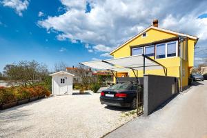 a yellow house with a car parked in a driveway at Apartment Loborika 1411 in Loborika