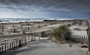 a fence on a sandy beach with the ocean at Nuits Salines Salin de Giraud in Salin-de-Giraud