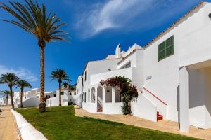 a white building with a palm tree in front of it at Vibra Blanc Cottage Apartmentos - 3SUP in Sa Caleta