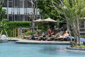 Sea View High Flr,2 Bed Room Exclusive At Pattaya في جنوب باتايا: مجموعة من الناس يجلسون في كراسي الحديقة بجانب حمام السباحة