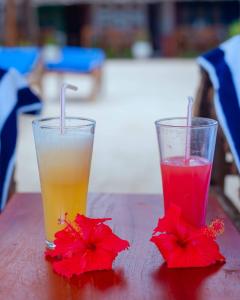two drinks are sitting on a table with red flowers at Suda Beach Lodge in Kumba Urembo