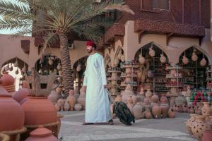 un uomo in piedi davanti a un negozio con una valigia di فندق المدينة القديمة Old Town Hotel a Nizwa