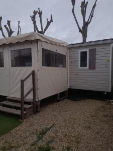 un gran remolque blanco con una tienda junto a algunos árboles en MOBIL HOME la STEPHANOISE, en Valras-Plage