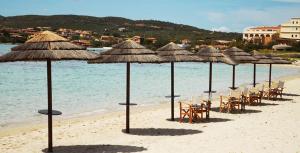 eine Reihe von Strohschirmen und -stühlen am Strand in der Unterkunft Hotel Patti in Golfo Aranci