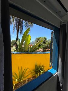 a window view of a yellow wall with plants at Casa dos franceses guesthouse ilha grande in Abraão