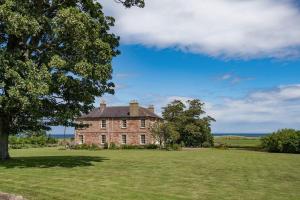a large brick house in a field with trees at East House in Berwick-Upon-Tweed