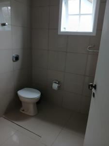 a white bathroom with a toilet and a window at Paraíso de Verão - Disfrute final de semana em Casa Exclusiva com piscina, sinuca e churrasqueira Aluguel para temporada em Riviera de São Lourenço in Bertioga