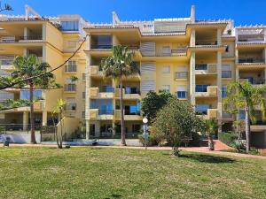 a large yellow building with palm trees in front of it at Two bedroom apartment with pool & sea views in Mijas Costa