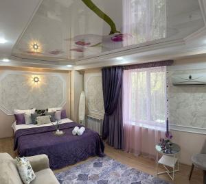 a bedroom with a bed with purple sheets and a couch at Уютный уголок in Shymkent
