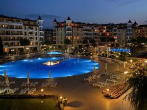 a large swimming pool with chairs and buildings at night at Apartment at Royal Sun, Sunny Beach in Sunny Beach