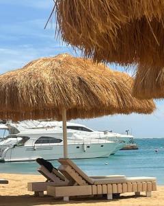 a straw umbrella and chairs on a beach with a boat at princess Resort Hurghada in Hurghada