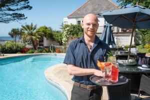 a man holding a tray with drinks on a table next to a pool at The White House Hotel in Herm