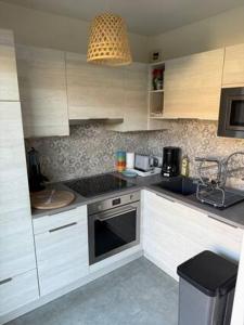 eine Küche mit weißen Schränken und einem Herd mit Backofen in der Unterkunft Cabourg, T2 jardin proche plage in Cabourg