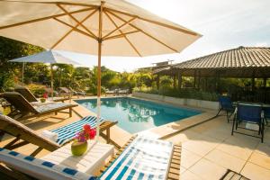 a swimming pool with an umbrella and chairs and a table at Pousada Jardim Cambuí Beach in Itacimirim