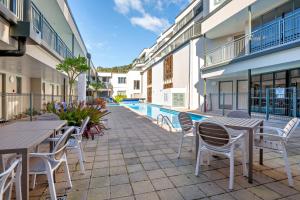 a patio with tables and chairs next to a pool at Beachpoint Apartments in Ohope Beach