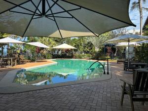 a swimming pool with an umbrella and tables and chairs at Wongalinga Beachfront Apt 2 in Mission Beach