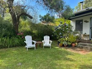 two white chairs and a table in a yard at Cosy retro styled bungalow in Narrawallee