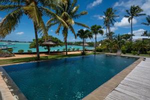 a swimming pool with palm trees and the ocean at 4- Bedroom Beachfront Villa in Grand Baie